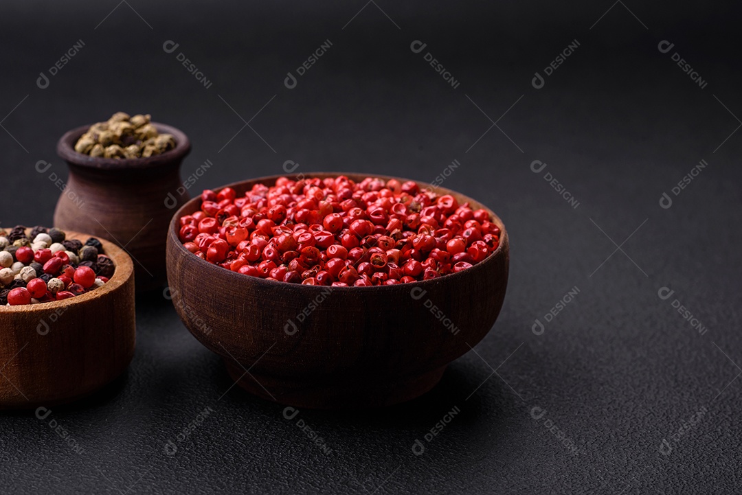 Composição, conceito, consistindo em vários tipos de cores diferentes de pimenta da Jamaica em tigelas e colheres sobre fundo escuro de concreto