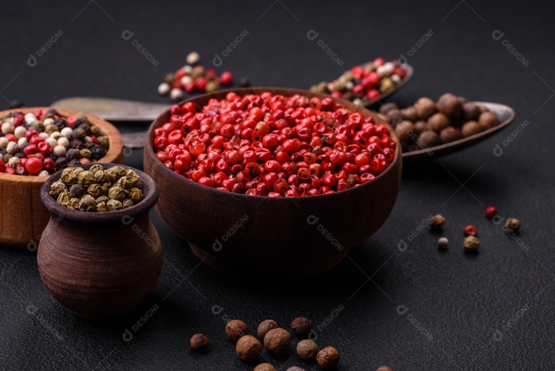 Composição, conceito, consistindo em vários tipos de cores diferentes de pimenta da Jamaica em tigelas e colheres sobre fundo escuro de concreto