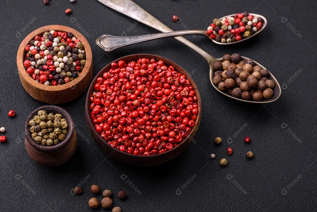 Composição, conceito, consistindo em vários tipos de cores diferentes de pimenta da Jamaica em tigelas e colheres sobre fundo escuro de concreto