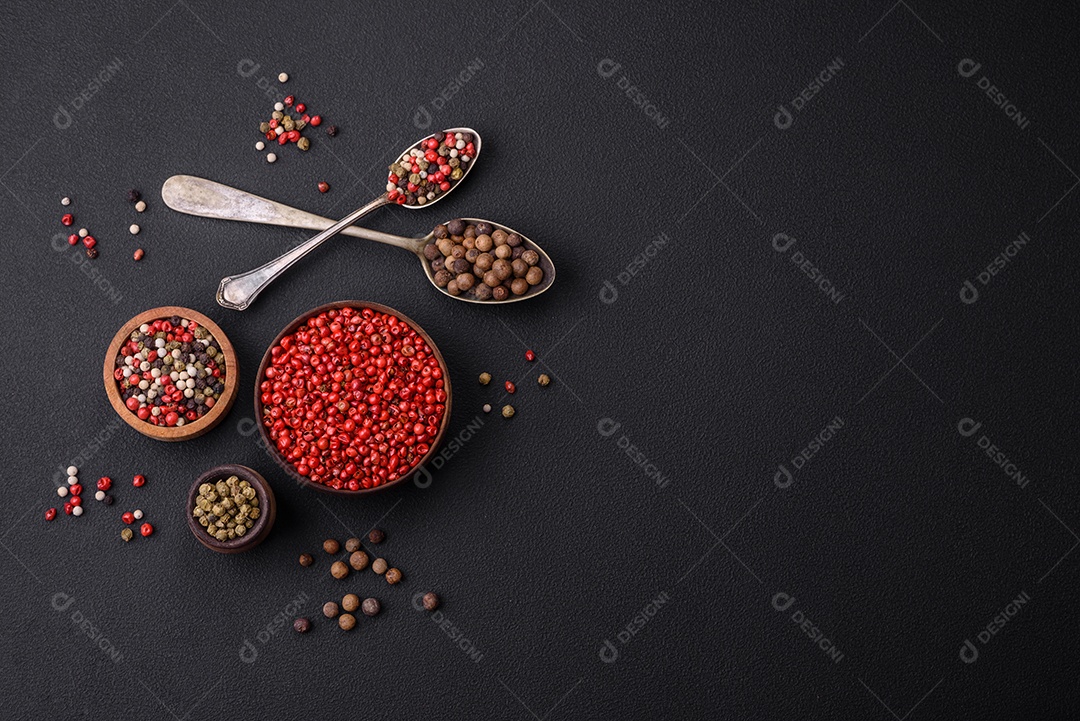 Composição, conceito, consistindo em vários tipos de cores diferentes de pimenta da Jamaica em tigelas e colheres sobre fundo escuro de concreto