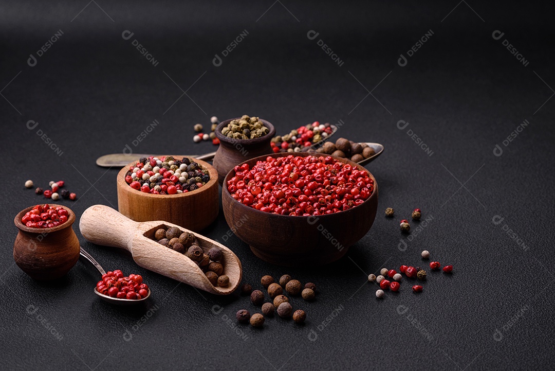Composição, conceito, consistindo em vários tipos de cores diferentes de pimenta da Jamaica em tigelas e colheres sobre fundo escuro de concreto