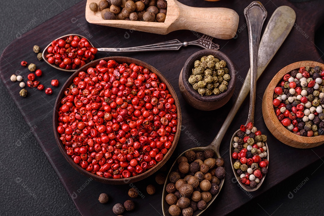 Composição, conceito, consistindo em vários tipos de cores diferentes de pimenta da Jamaica em tigelas e colheres sobre fundo escuro de concreto