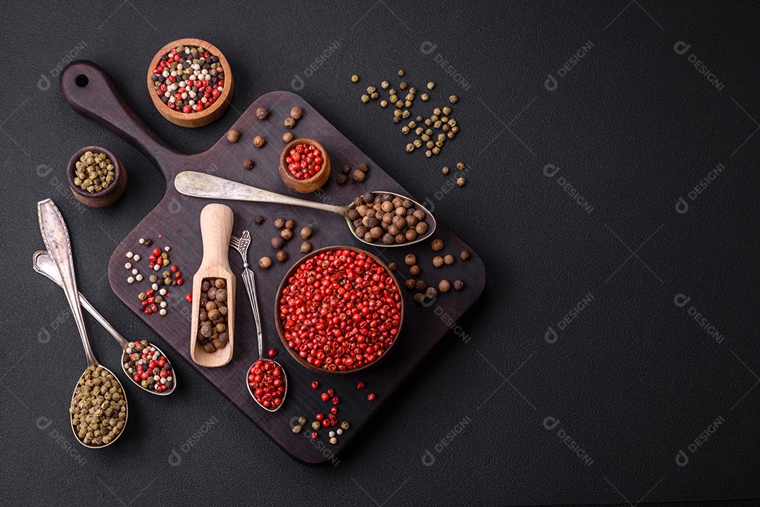 Composição, conceito, consistindo em vários tipos de cores diferentes de pimenta da Jamaica em tigelas e colheres sobre fundo escuro de concreto