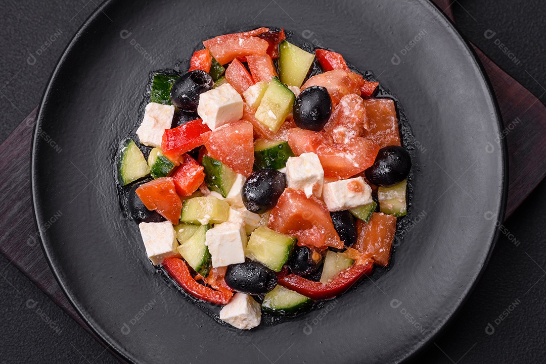 Deliciosa salada grega fresca com azeitonas, tomates, pepinos, queijo feta, especiarias, ervas e azeite num prato cerâmico preto