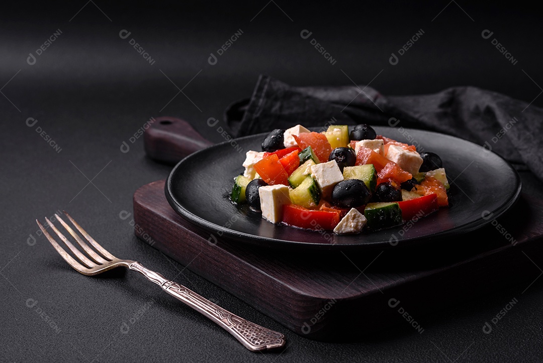 Deliciosa salada grega fresca com azeitonas, tomates, pepinos, queijo feta, especiarias, ervas e azeite num prato cerâmico preto