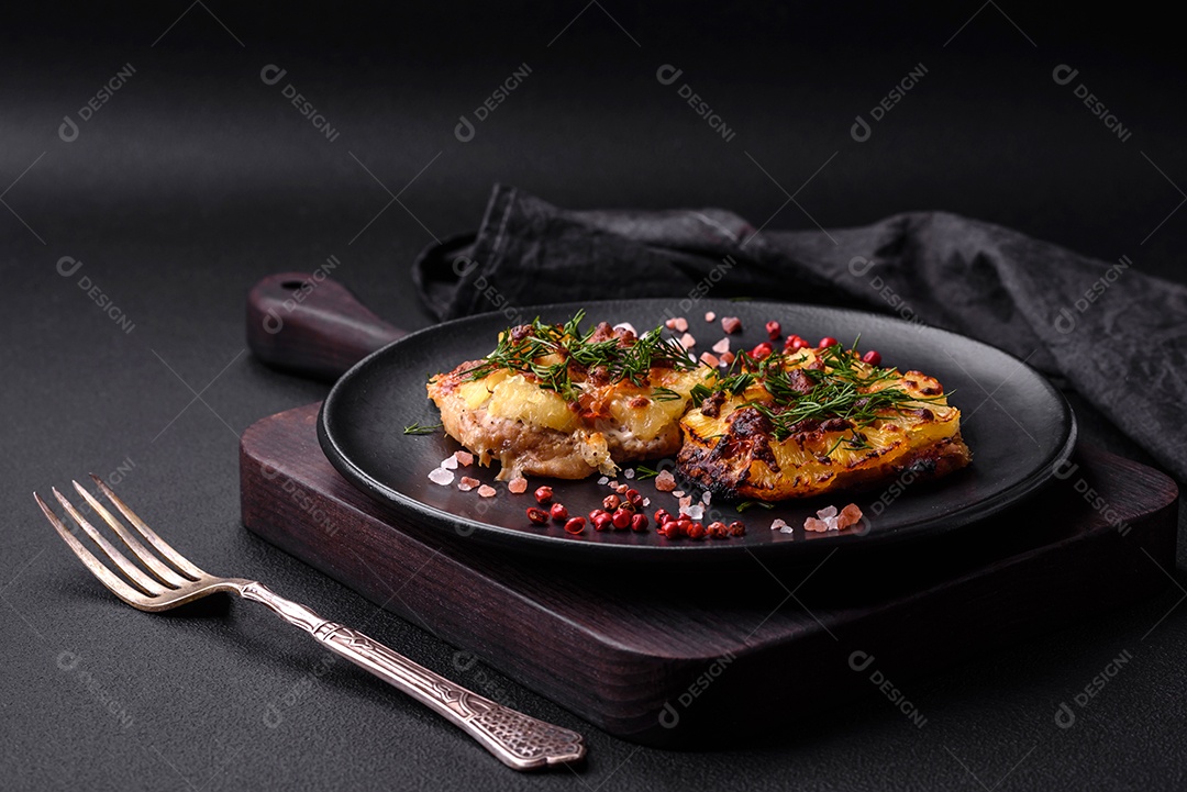 Carne assada no forno com abacaxi, tomate, queijo, especiarias e ervas em uma placa de cerâmica preta sobre fundo escuro de concreto