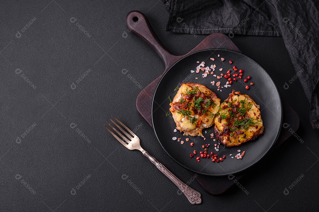 Carne assada no forno com abacaxi, tomate, queijo, especiarias e ervas em uma placa de cerâmica preta sobre fundo escuro de concreto