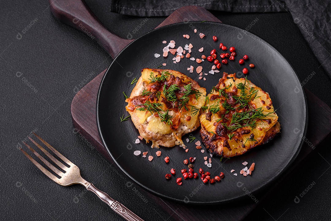 Carne assada no forno com abacaxi, tomate, queijo, especiarias e ervas em uma placa de cerâmica preta sobre fundo escuro de concreto