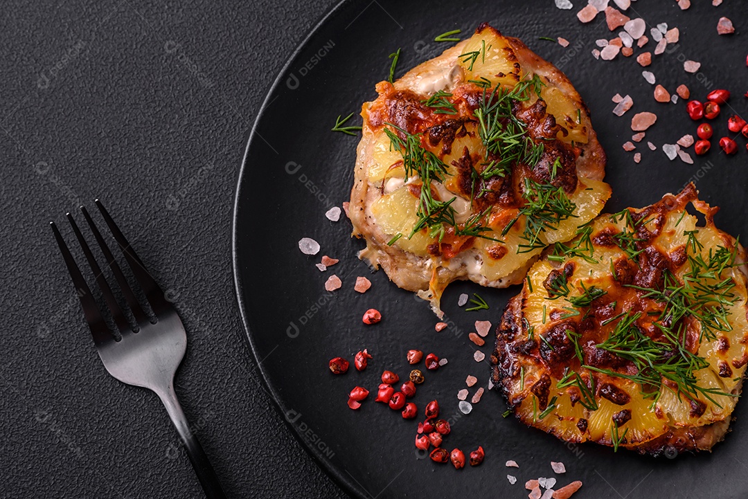 Carne assada no forno com abacaxi, tomate, queijo, especiarias e ervas em uma placa de cerâmica preta sobre fundo escuro de concreto
