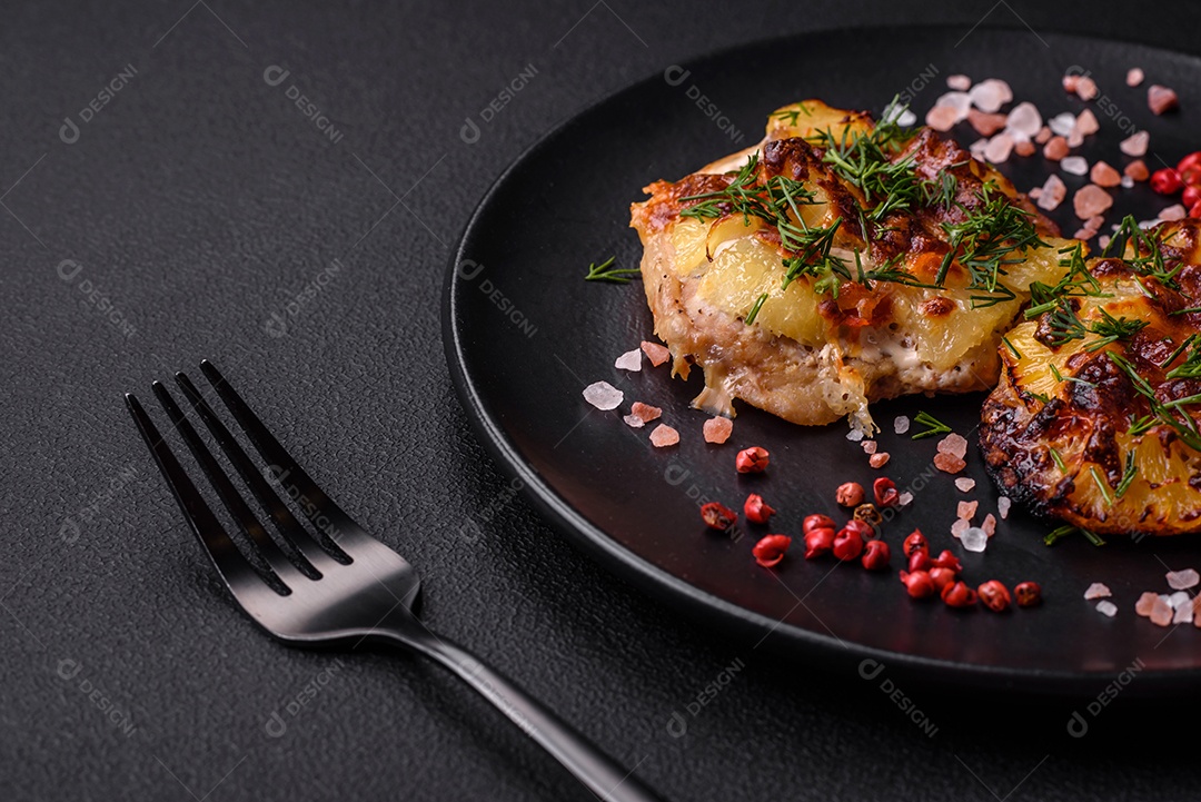 Carne assada no forno com abacaxi, tomate, queijo, especiarias e ervas em uma placa de cerâmica preta sobre fundo escuro de concreto