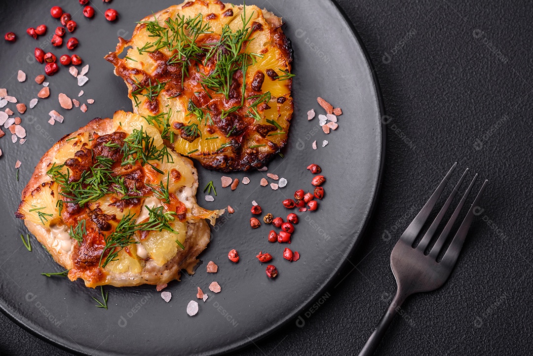 Carne assada no forno com abacaxi, tomate, queijo, especiarias e ervas em uma placa de cerâmica preta sobre fundo escuro de concreto