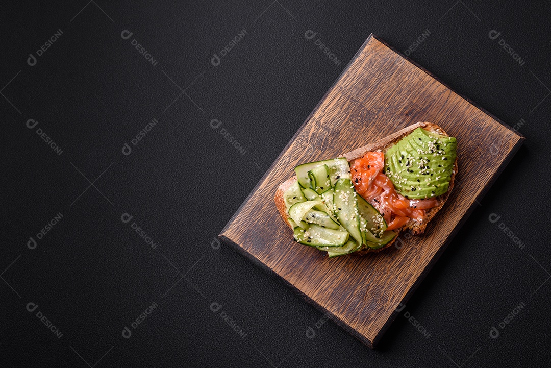 Deliciosa torrada de pão integral com sementes de salmão, abacate, pepino e gergelim sobre um fundo de concreto texturizado