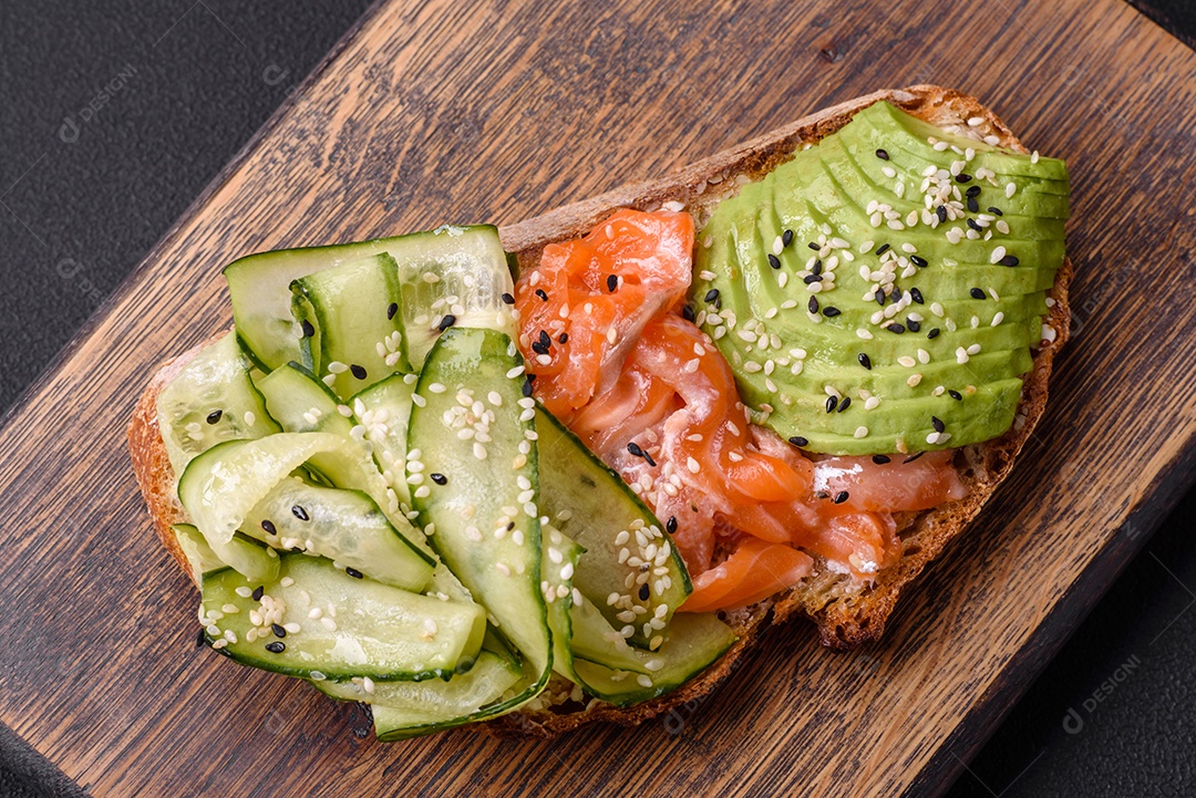 Deliciosa torrada de pão integral com sementes de salmão, abacate, pepino e gergelim sobre um fundo de concreto texturizado