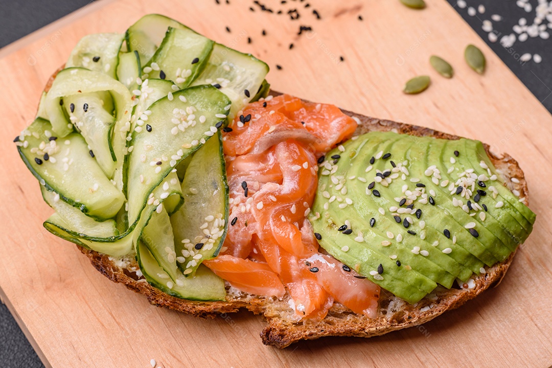 Deliciosa torrada de pão integral com sementes de salmão, abacate, pepino e gergelim sobre um fundo de concreto texturizado