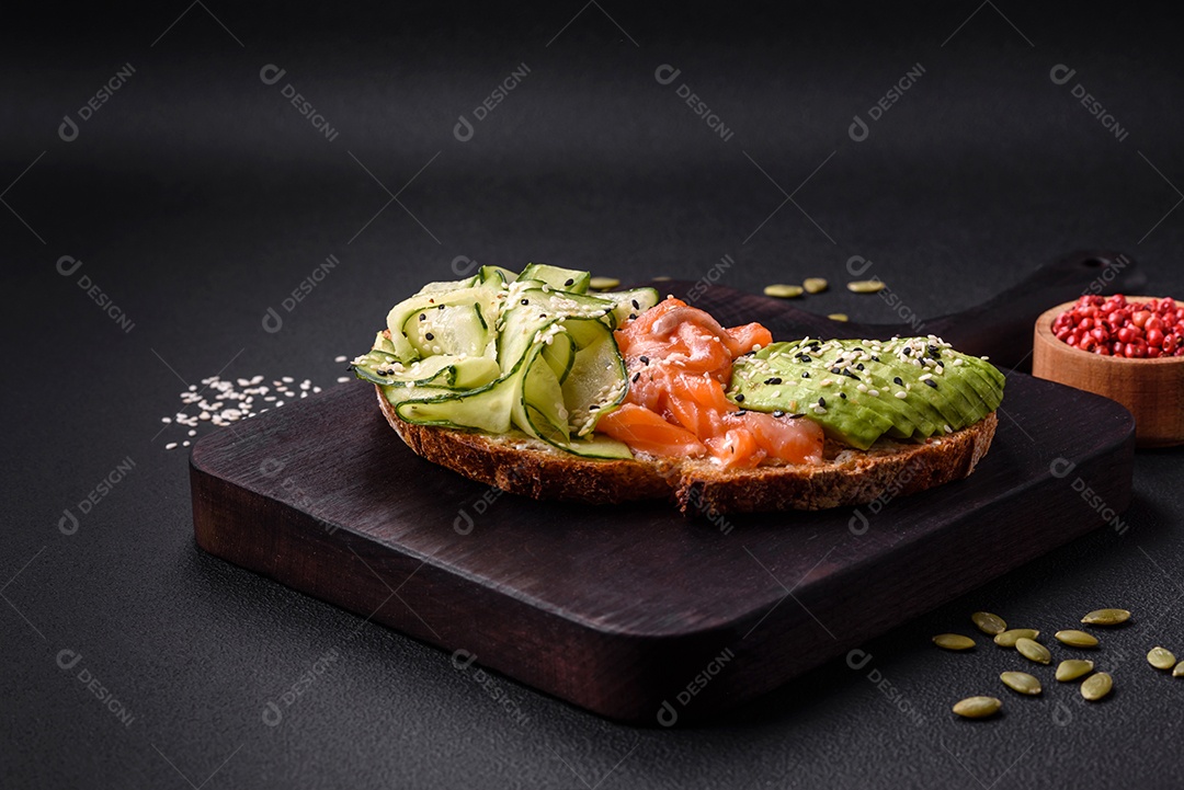 Deliciosa torrada de pão integral com sementes de salmão, abacate, pepino e gergelim sobre um fundo de concreto texturizado