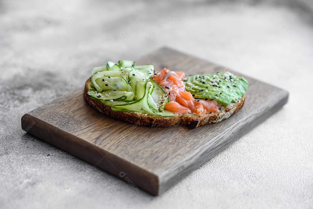 Deliciosa torrada de pão integral com sementes de salmão, abacate, pepino e gergelim sobre um fundo de concreto texturizado