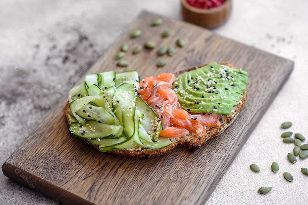 Deliciosa torrada de pão integral com sementes de salmão, abacate, pepino e gergelim sobre um fundo de concreto texturizado