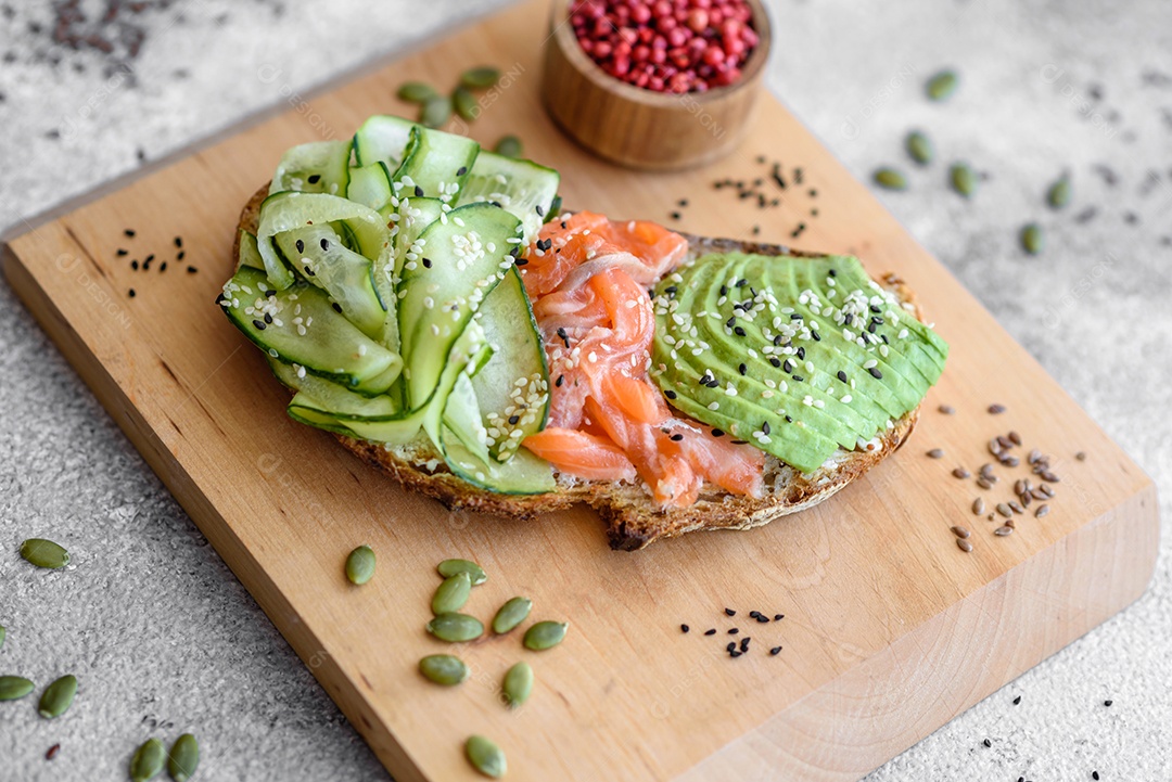 Deliciosa torrada de pão integral com sementes de salmão, abacate, pepino e gergelim sobre um fundo de concreto texturizado