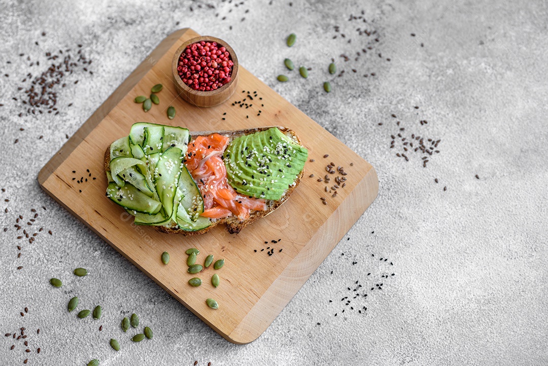 Deliciosa torrada de pão integral com sementes de salmão, abacate, pepino e gergelim sobre um fundo de concreto texturizado