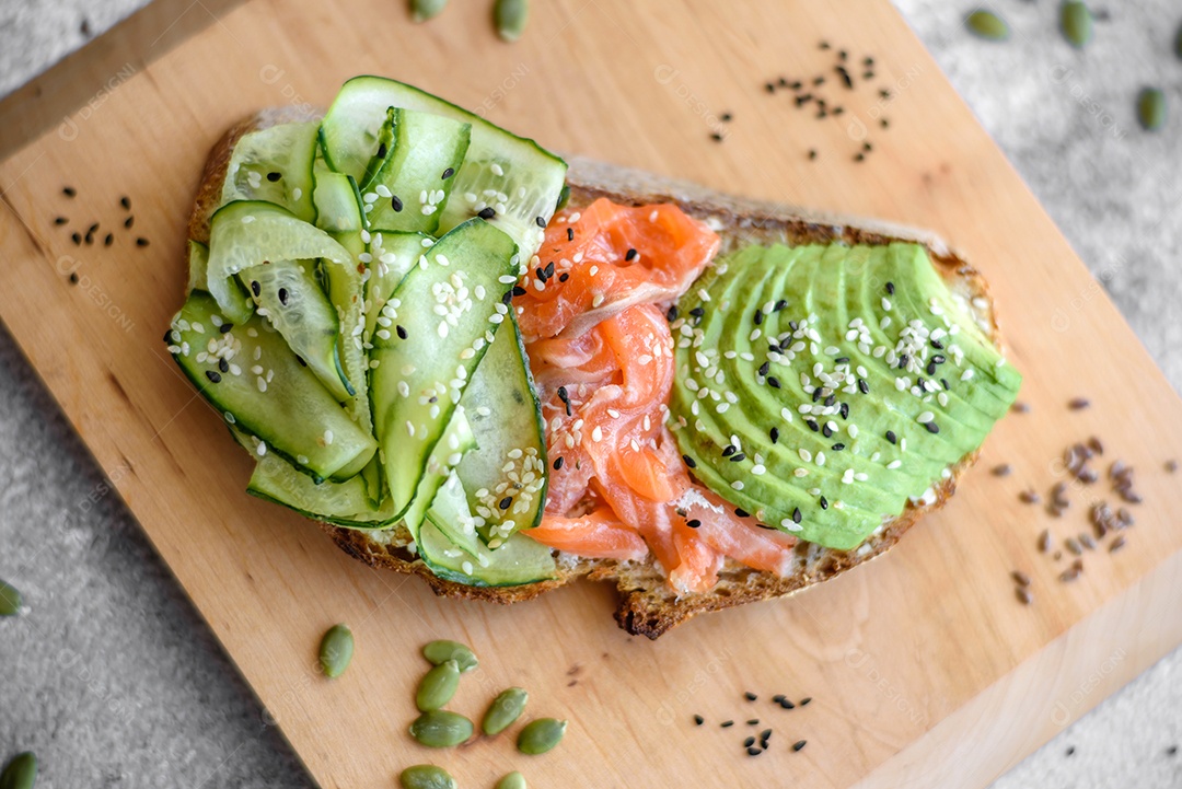 Deliciosa torrada de pão integral com sementes de salmão, abacate, pepino e gergelim sobre um fundo de concreto texturizado
