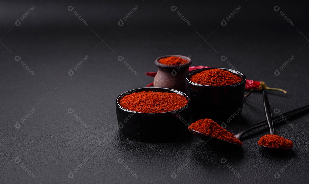 Tempere a páprica defumada em forma de pó em tigelas e colheres sobre um fundo escuro de concreto. Ingredientes da culinária asiática