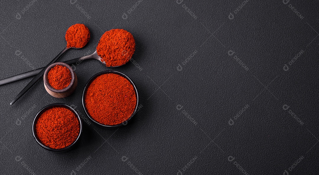 Tempere a páprica defumada em forma de pó em tigelas e colheres sobre um fundo escuro de concreto. Ingredientes da culinária asiática