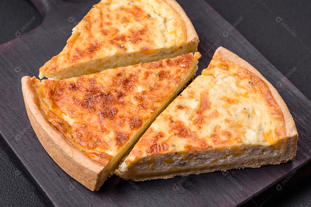 Linda e deliciosa torta de quiche com quatro tipos de queijo com especiarias e ervas em um fundo escuro de concreto