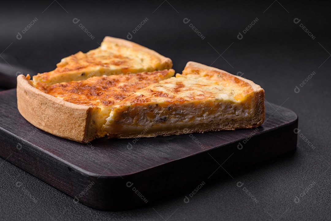 Linda e deliciosa torta de quiche com quatro tipos de queijo com especiarias e ervas em um fundo escuro de concreto