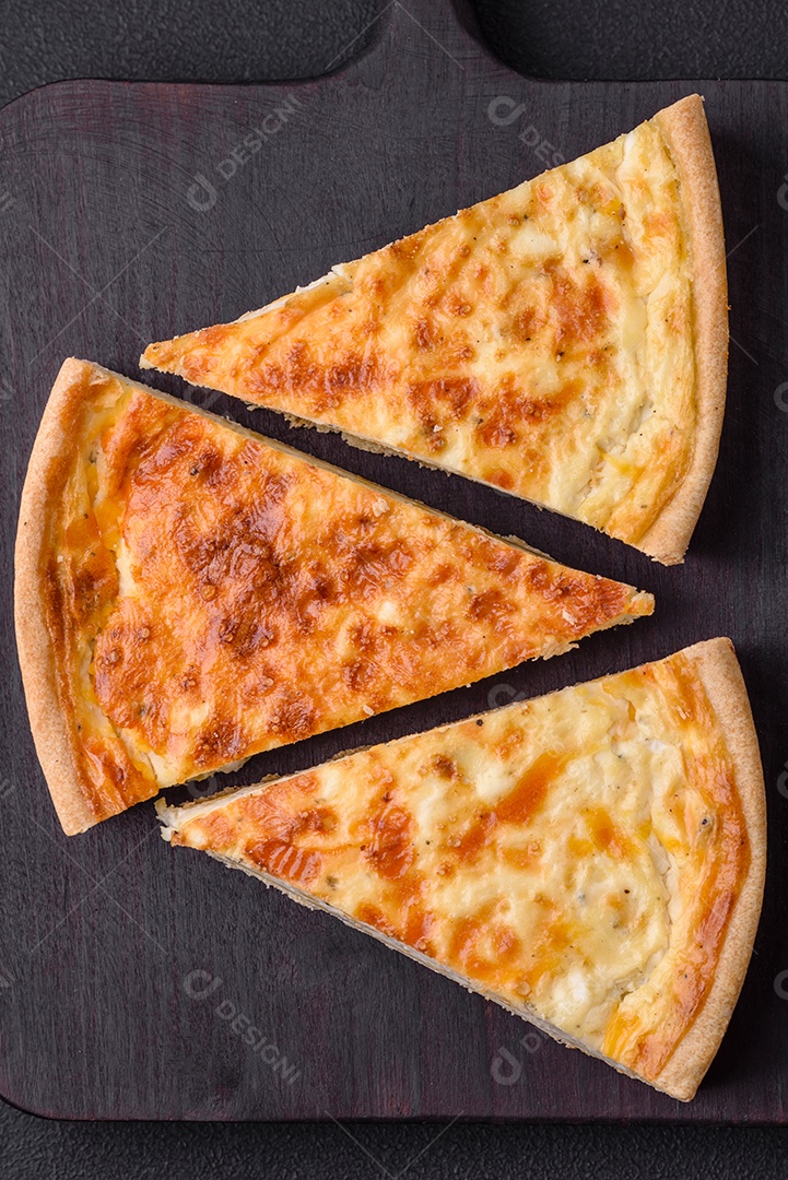 Linda e deliciosa torta de quiche com quatro tipos de queijo com especiarias e ervas em um fundo escuro de concreto