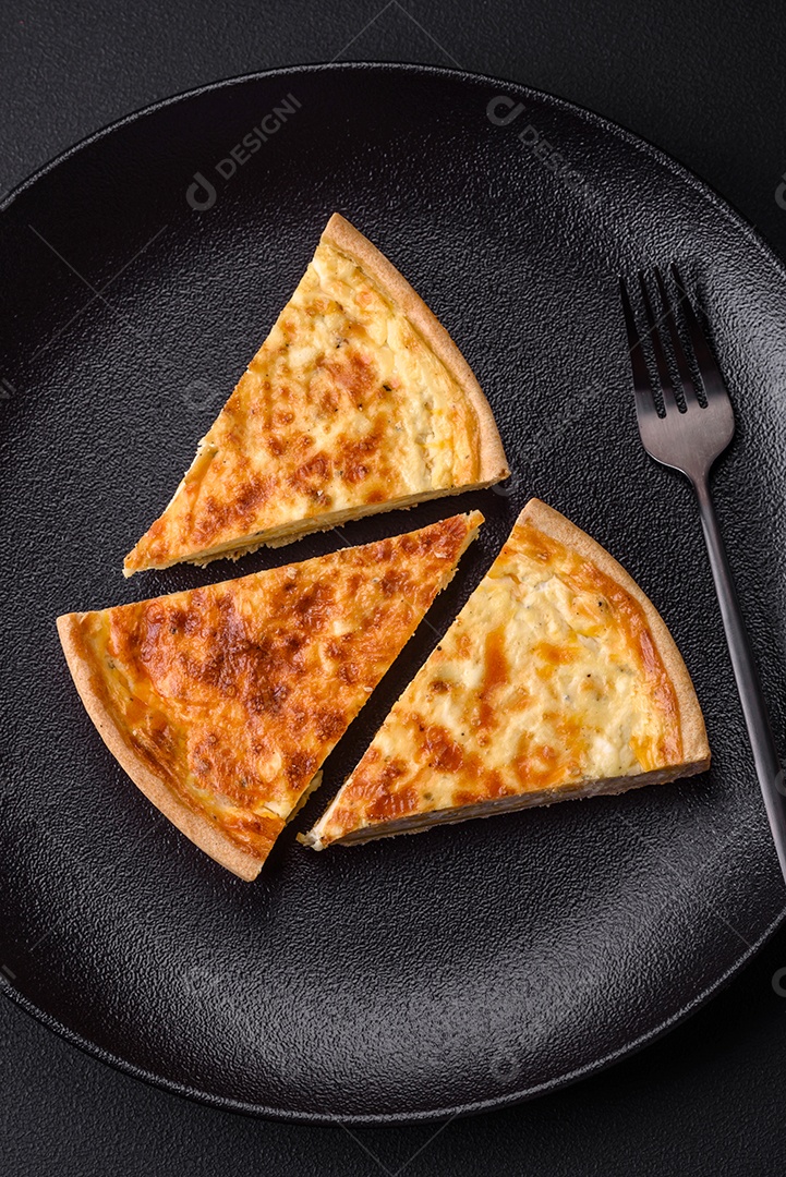Linda e deliciosa torta de quiche com quatro tipos de queijo com especiarias e ervas em um fundo escuro de concreto