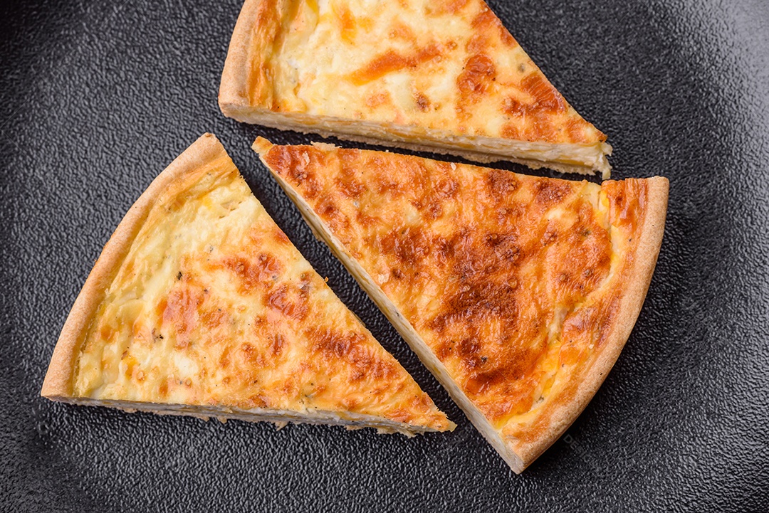 Linda e deliciosa torta de quiche com quatro tipos de queijo com especiarias e ervas em um fundo escuro de concreto