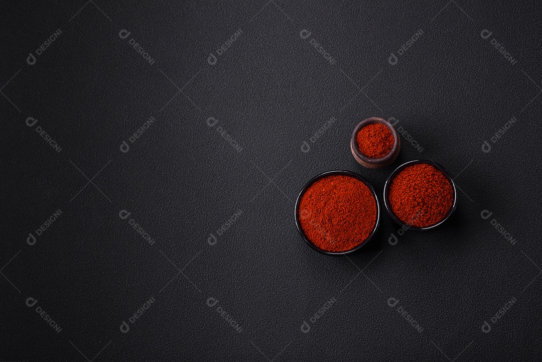 Tempere a páprica defumada em forma de pó em tigelas e colheres sobre um fundo escuro de concreto. Ingredientes da culinária asiática