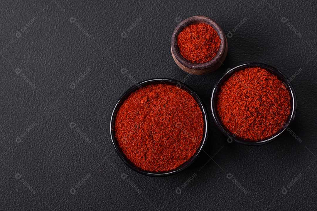 Tempere a páprica defumada em forma de pó em tigelas e colheres sobre um fundo escuro de concreto. Ingredientes da culinária asiática