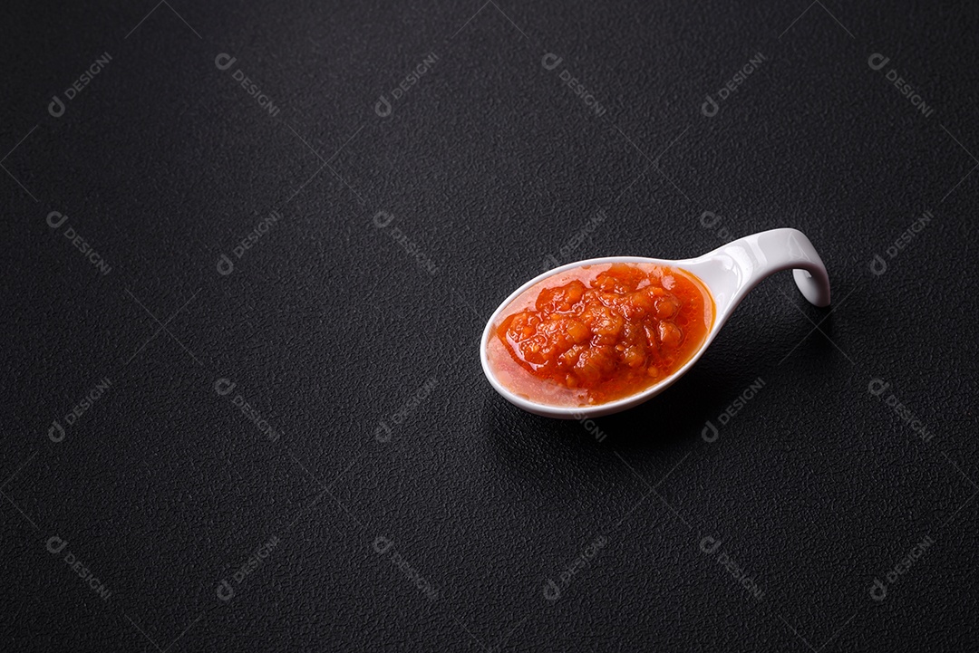 Molho adjika vermelho ou ketchup com especiarias e ervas sobre um fundo escuro de concreto