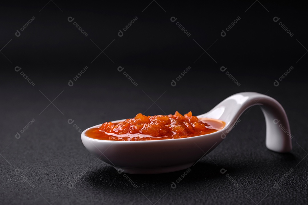 Molho adjika vermelho ou ketchup com especiarias e ervas sobre um fundo escuro de concreto