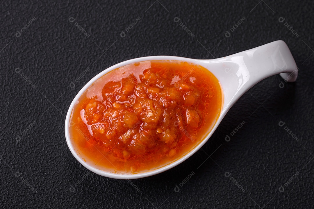 Molho adjika vermelho ou ketchup com especiarias e ervas sobre um fundo escuro de concreto