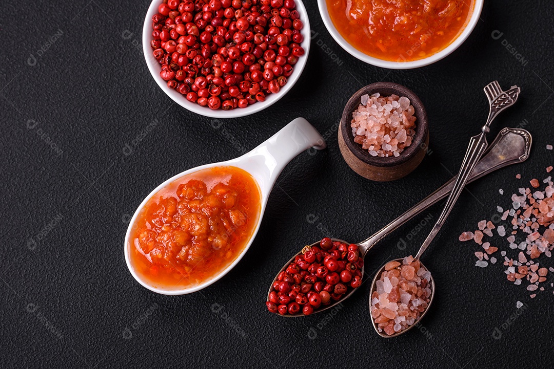 Molho adjika vermelho ou ketchup com especiarias e ervas sobre um fundo escuro de concreto