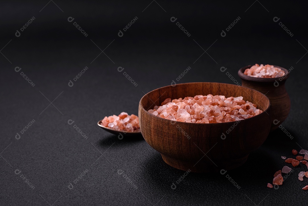 Sal rosa do Himalaia em uma tigela de madeira sobre um fundo escuro de concreto. Temperos e aditivos na cozinha