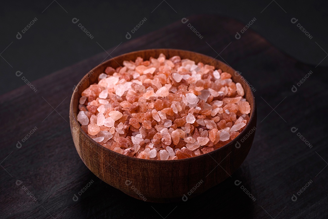 Sal rosa do Himalaia em uma tigela de madeira sobre um fundo escuro de concreto. Temperos e aditivos na cozinha
