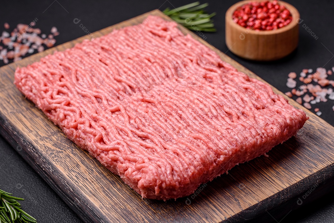 Carne crua ou carne de porco picada com especiarias salgadas e ervas em uma tábua de madeira sobre um fundo escuro de concreto