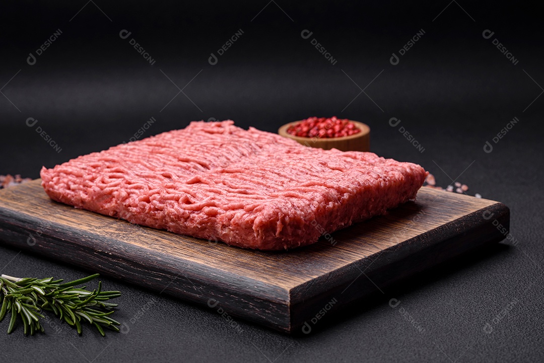 Carne crua ou carne de porco picada com especiarias salgadas e ervas em uma tábua de madeira sobre um fundo escuro de concreto