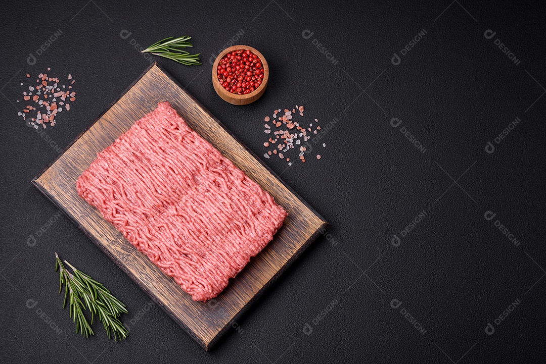 Carne crua ou carne de porco picada com especiarias salgadas e ervas em uma tábua de madeira sobre um fundo escuro de concreto