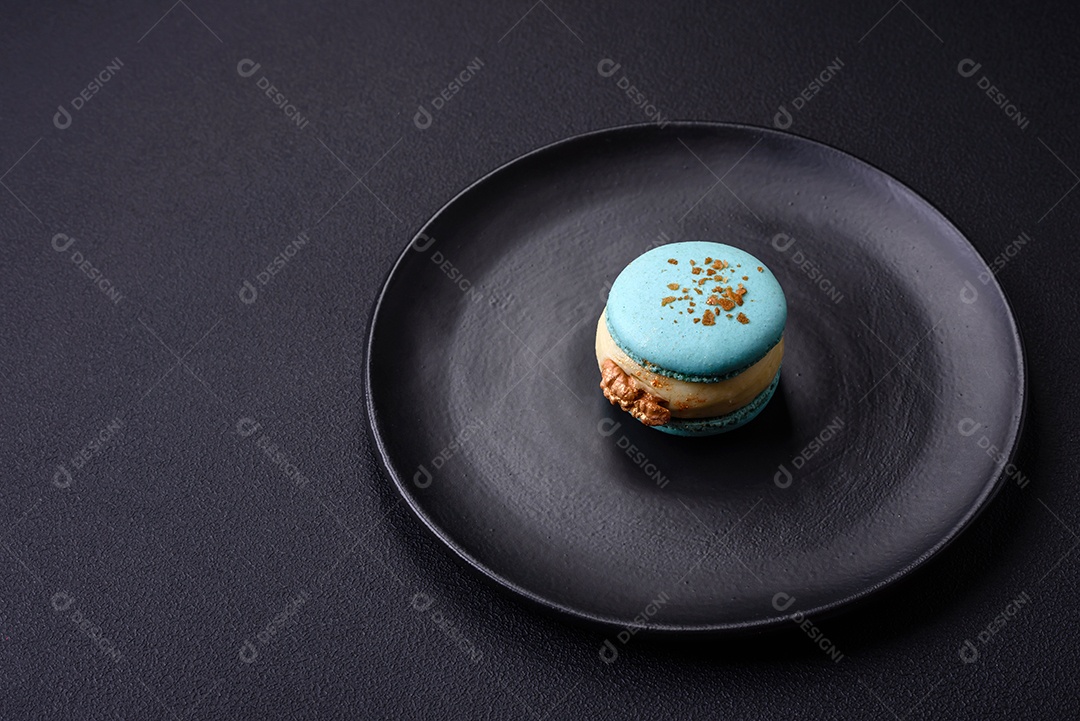 Lindo macaron saboroso com recheio e sabor de frutas em uma placa preta sobre um fundo escuro de concreto