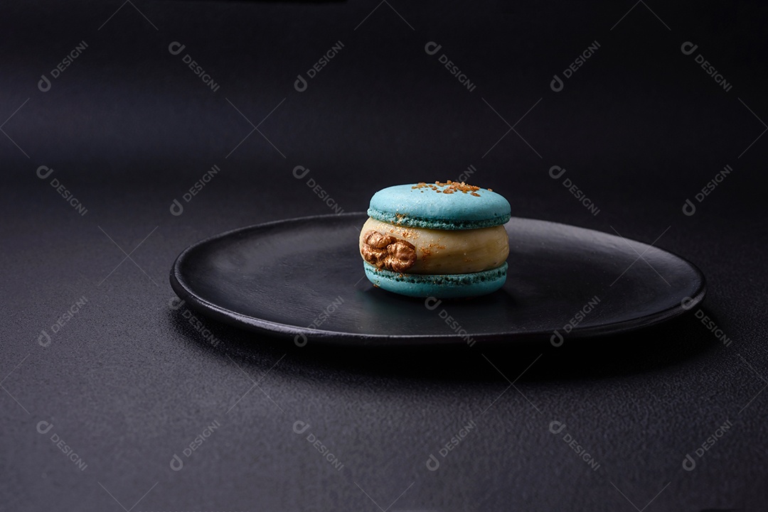 Lindo macaron saboroso com recheio e sabor de frutas em uma placa preta sobre um fundo escuro de concreto