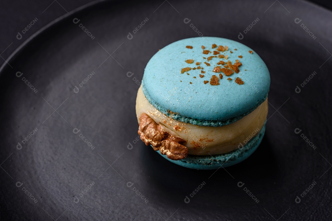 Lindo macaron saboroso com recheio e sabor de frutas em uma placa preta sobre um fundo escuro de concreto