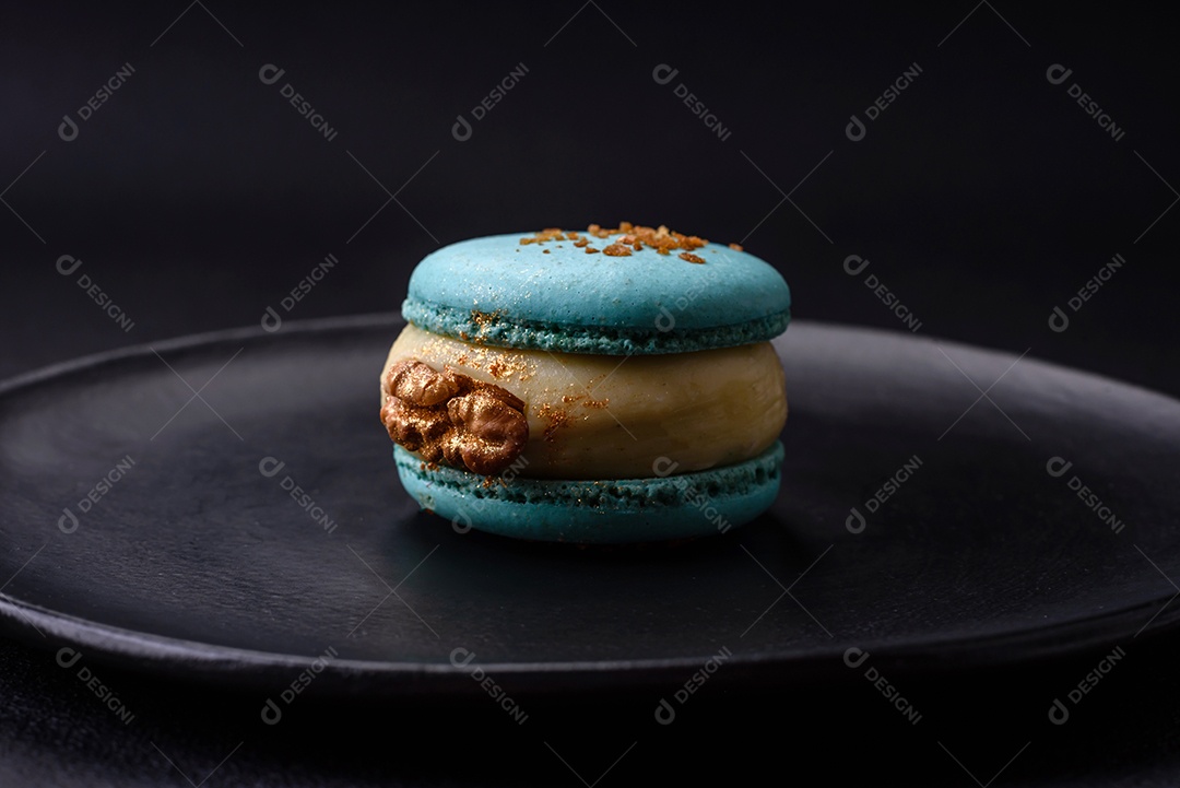 Lindo macaron saboroso com recheio e sabor de frutas em uma placa preta sobre um fundo escuro de concreto