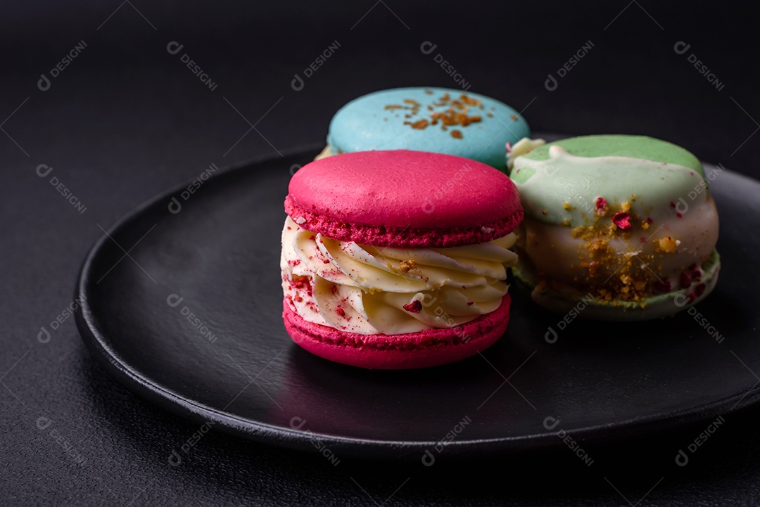 Lindo macaron saboroso com recheio e sabor de frutas em uma placa preta sobre um fundo escuro de concreto