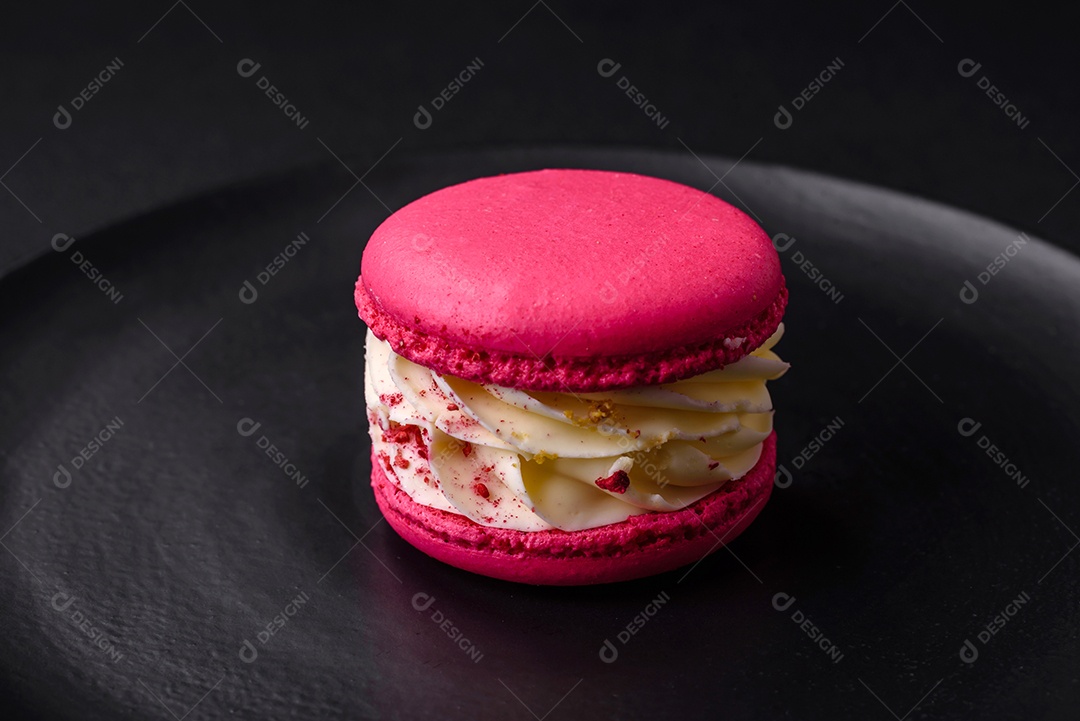 Lindo macaron saboroso com recheio e sabor de frutas em uma placa preta sobre um fundo escuro de concreto
