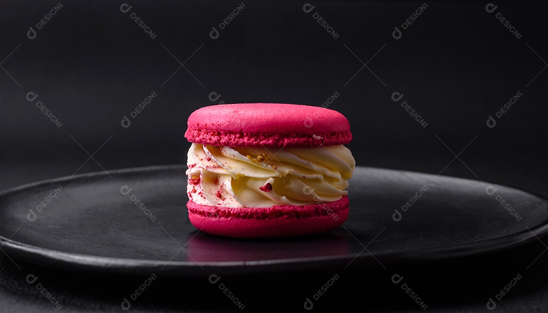Lindo macaron saboroso com recheio e sabor de frutas em uma placa preta sobre um fundo escuro de concreto