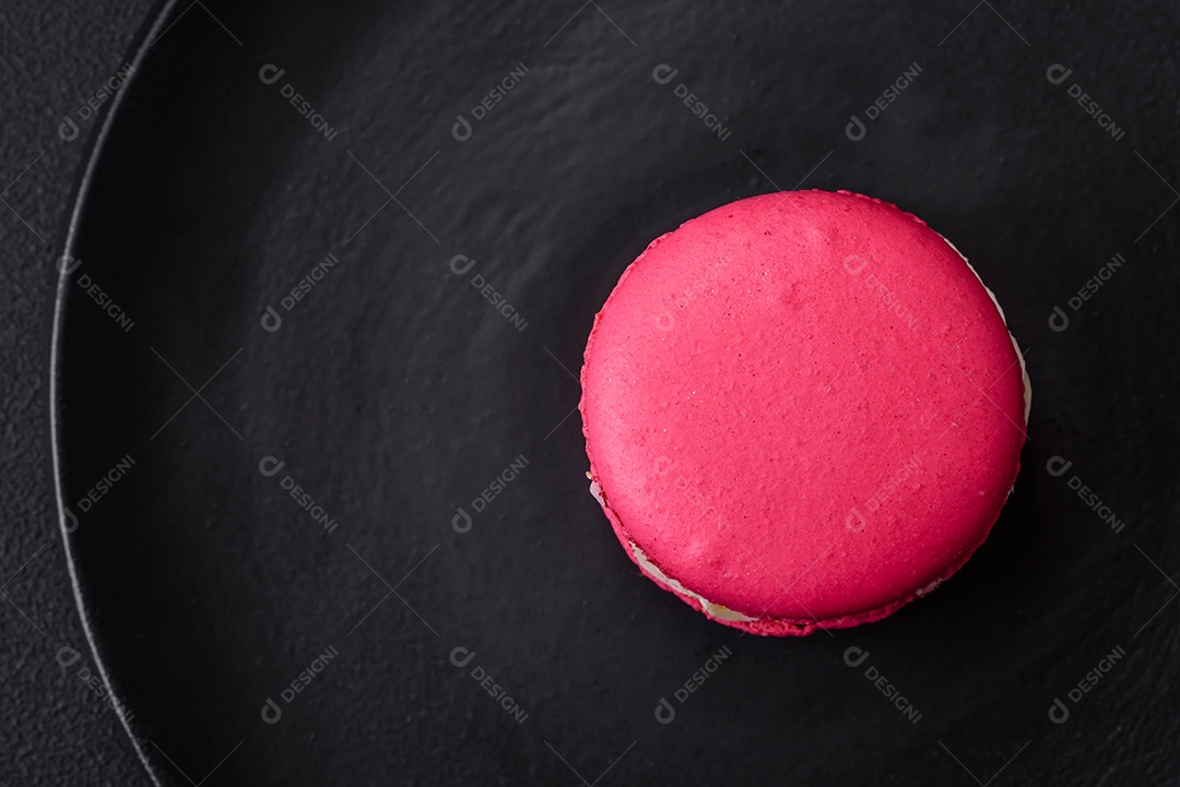 Lindo macaron saboroso com recheio e sabor de frutas em uma placa preta sobre um fundo escuro de concreto